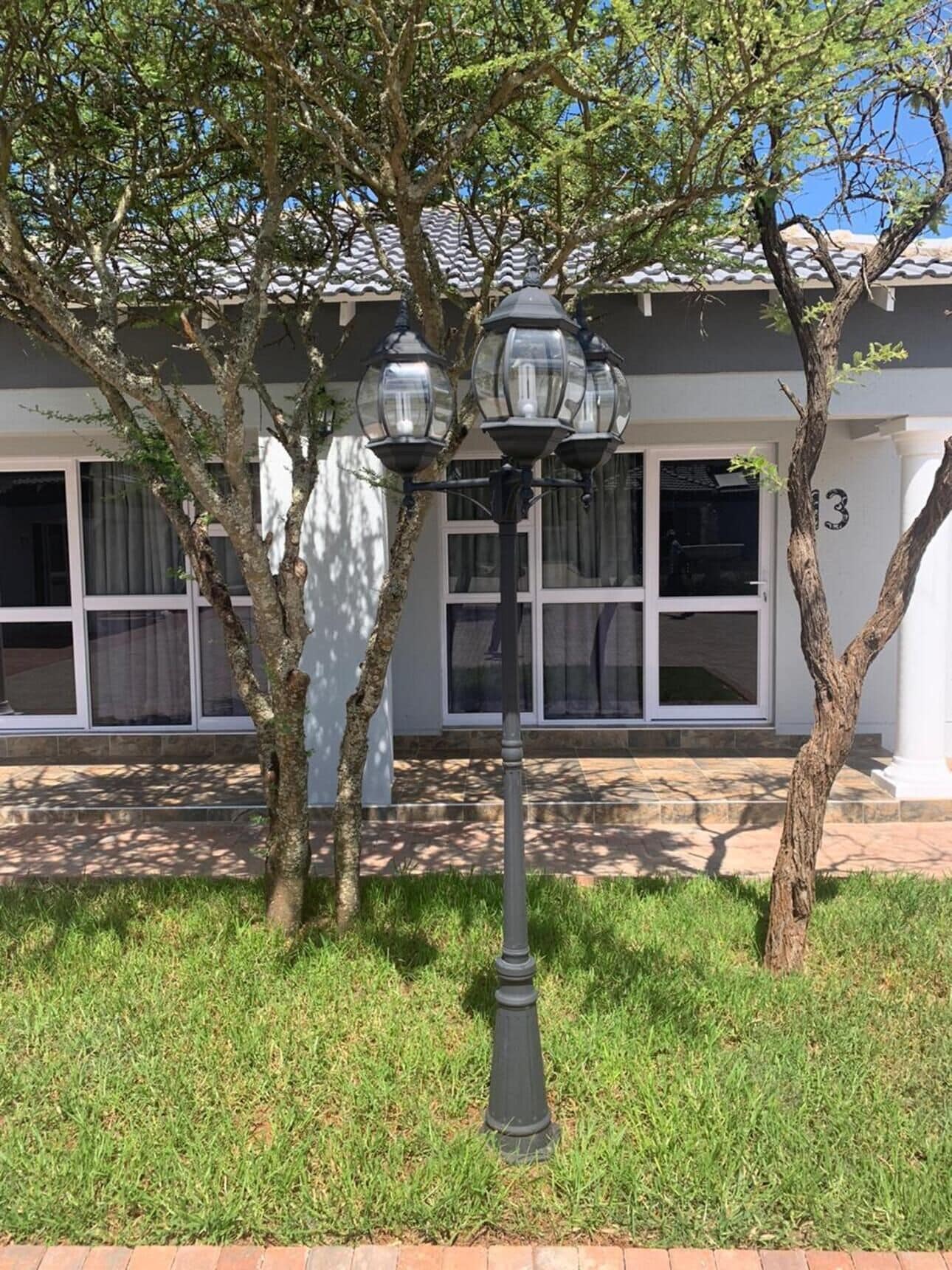 A street lamp with three globes, a tree, and a building with large windows and a number '13' on the wall.