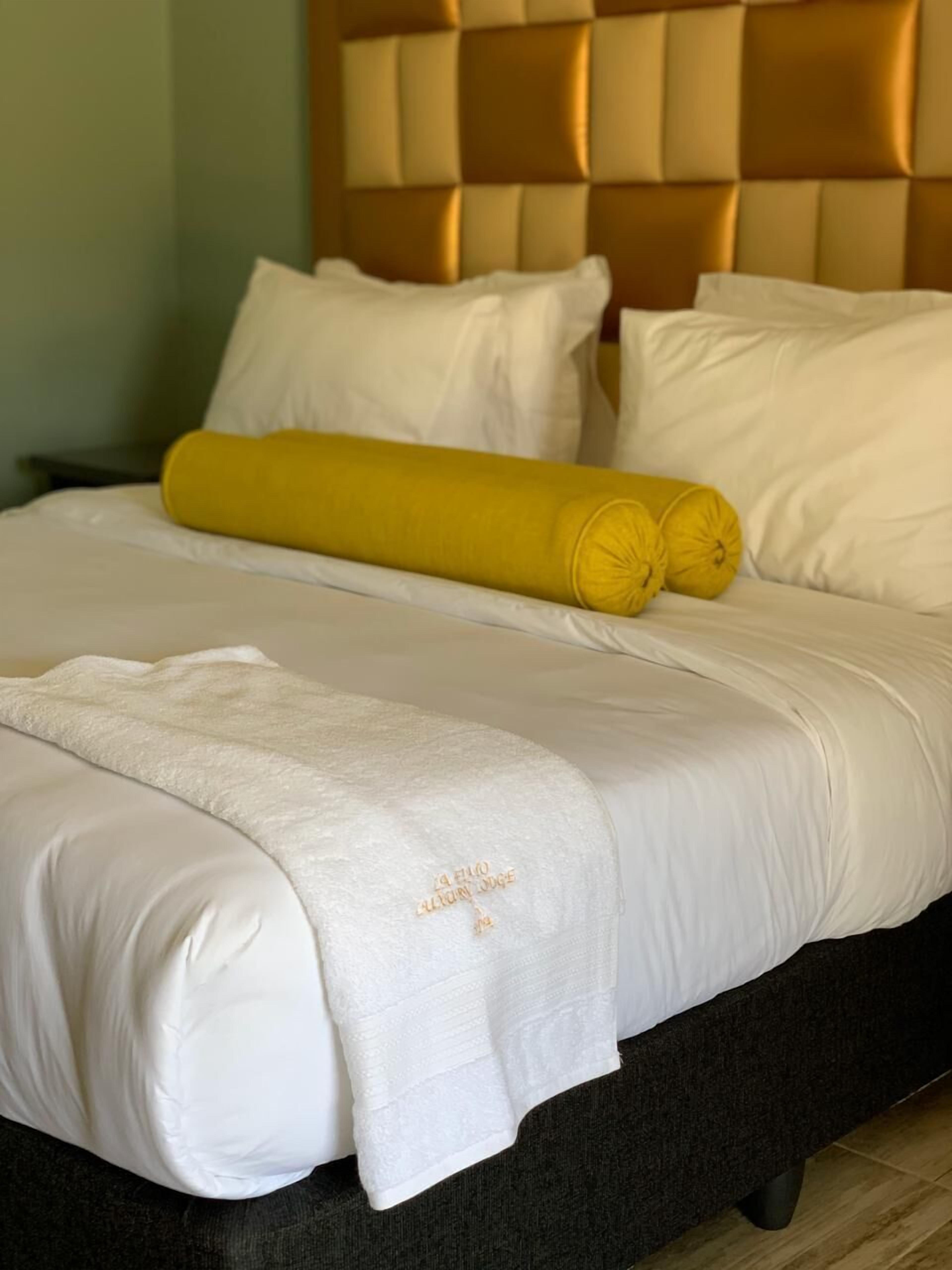 A neatly made bed with white linens, a yellow rolled blanket, and a matching pillow.