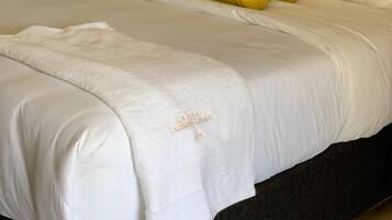A neatly made bed with white linens, a yellow rolled blanket, and a matching pillow.