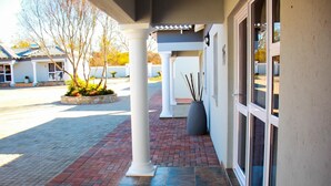 A hotel entrance with a covered walkway, a stone planter with plants, and a large vase with sticks. - La Fiato Luxury Lodge (Polokwane)