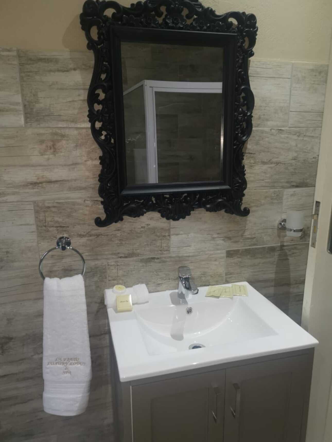 A bathroom with a white sink, a mirror with an ornate black frame, and a towel rack with a white towel.