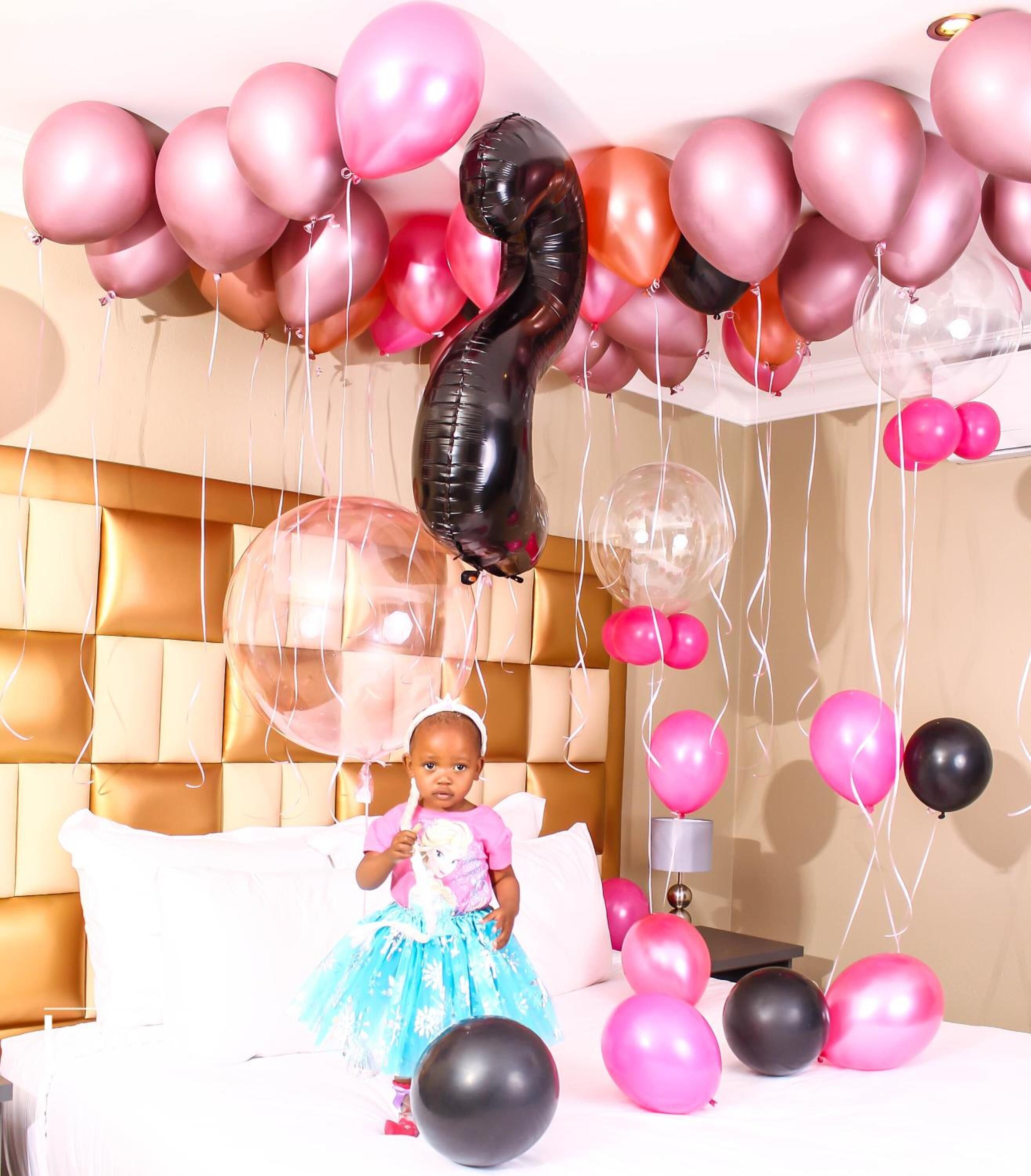 A room with a bed, a headboard, and a variety of balloons.