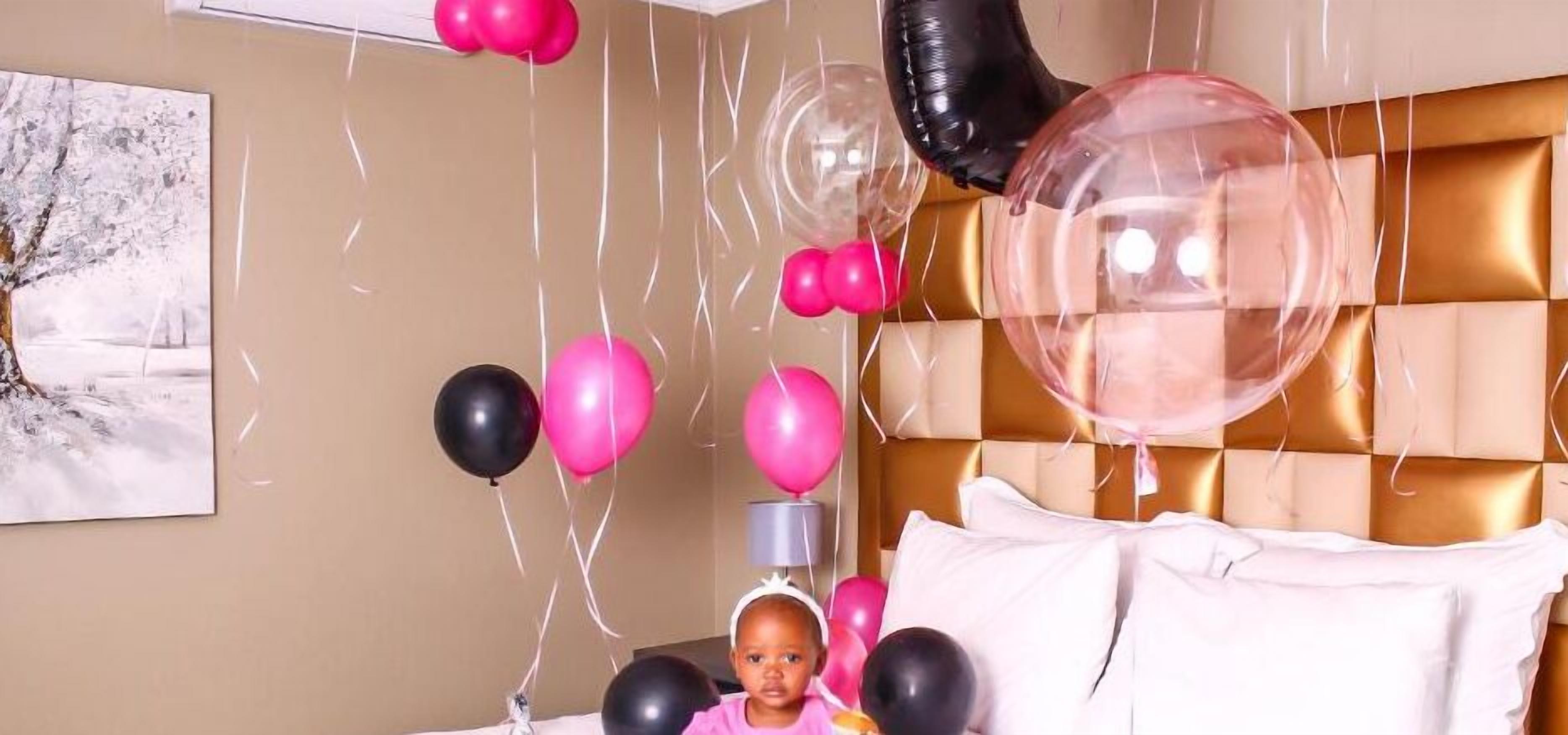 A room with a bed, a wall-mounted painting, and balloons.