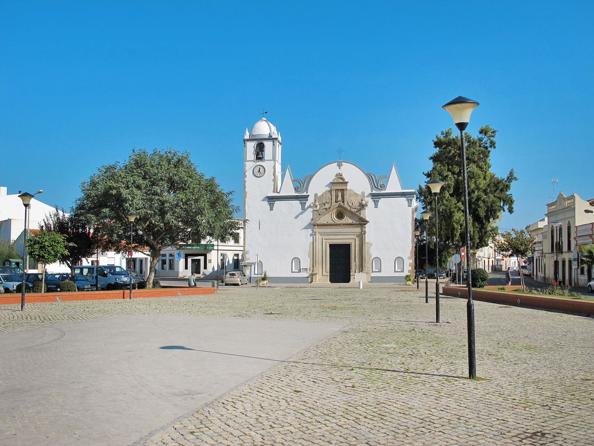 Une église historique dotée d’un clocher et d’un dôme central, entourée de rues pavées et d’arbres.
