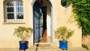 A building entrance with a blue door, a window with metal bars, and two potted plants. - Marina Petite Belge à Aigues Mortes (incl city bikes on request) (Aigues-Mortes)