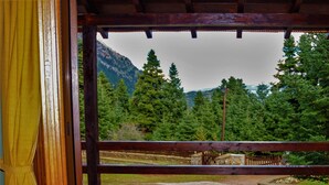 Eine terrasse mit steinbelagtem Boden und Holzwertkasten, mit Blick auf ein bewaldetes Gebirge, und ein gelber Vorhang ist an der linken Seite teilweise sichtbar.