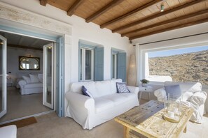 Ein weißes Sofa mit blauen Fensterläden, ein Holztisch und Blick auf eine felsige Landschaft durch ein großes Fenster.