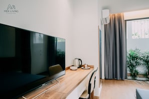 Relax in this stylish room with a large flat-screen TV, dining table, and comfortable chair, offering a view of lush greenery outside.