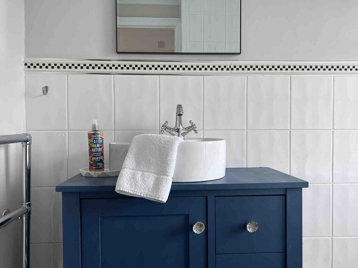 Une salle de bain avec un lavabo blanc, un meuble bleu, une serviette et un flacon de savon pour les mains.