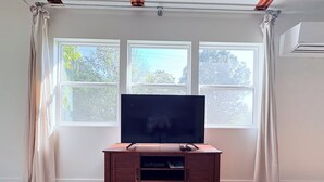 Una habitación con un mueble de madera que sirve como centro de entretenimiento, un televisor de pantalla plana y un gran ventanal con cortinas.