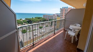 Un balcon avec vue sur la mer, un espace délimité par une clôture et des chaises en plastique blanches.