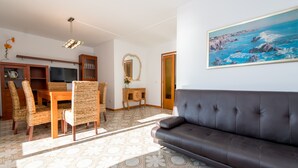 Un salon avec un canapé en cuir marron, une table à manger entourée de chaises en osier, un téléviseur et un tableau encadré accroché au mur.
