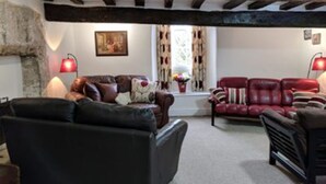 A cozy living room with a stone fireplace, leather sofas, and red lamps. - Cotswolds Valleys Accommodation-Med Hall (Stroud)