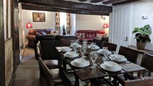 A dining area with a long wooden table set for a meal, flanked by chairs. - Cotswolds Valleys Accommodation-Med Hall (Stroud)