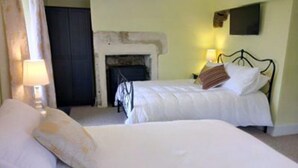 A bedroom with two beds, a fireplace, and a wall-mounted TV. - Cotswolds Valleys Accommodation-Med Hall (Stroud)