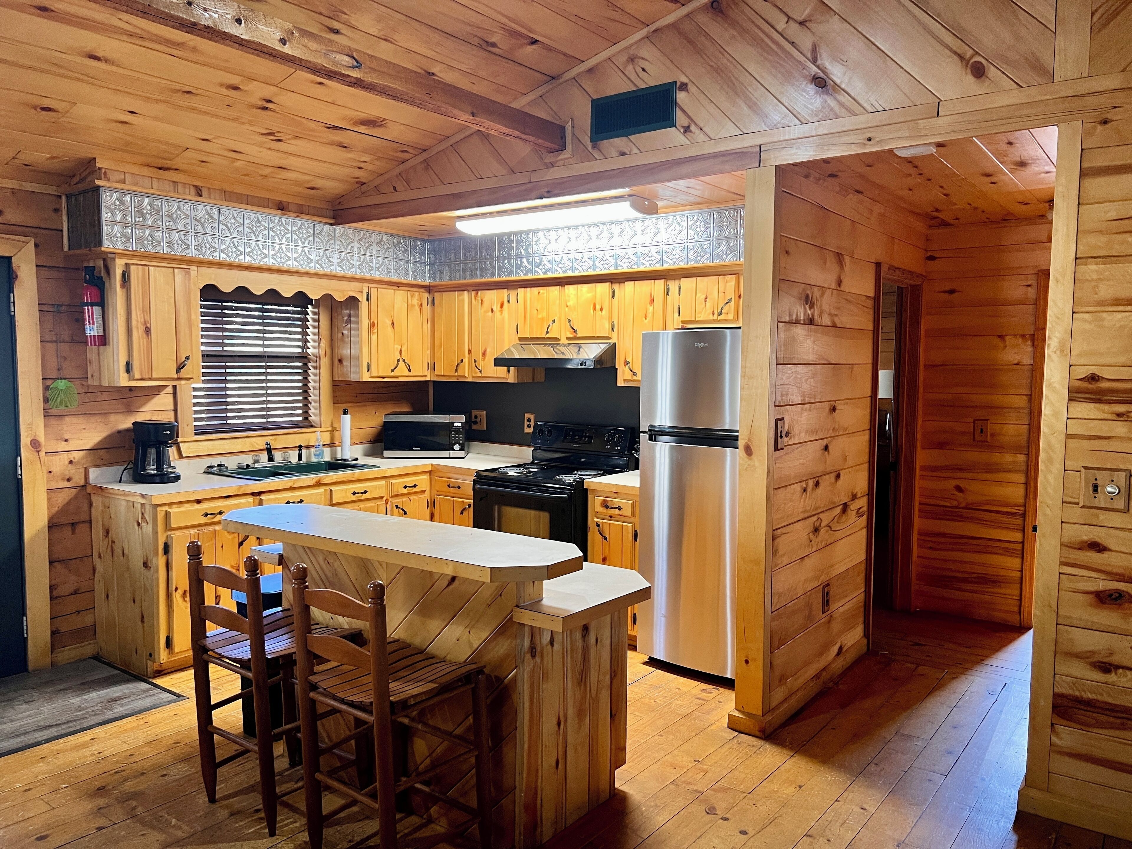 Une cuisine rustique, située dans une cabane en bois, avec un îlot central, des armoires en bois, un réfrigérateur en acier inoxydable et une cuisinière.