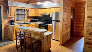 A wooden cabin kitchen with a central island, wooden cabinets, a stainless steel refrigerator, and a stove.