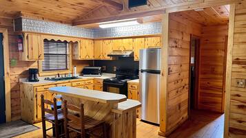 Une cuisine rustique, située dans une cabane en bois, avec un îlot central, des armoires en bois, un réfrigérateur en acier inoxydable et une cuisinière.