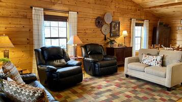 A cozy cabin interior with wooden walls, two leather chairs, a white sofa, and a patterned rug.