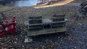 A lakeside area with a wooden bench, a small dock, and a cabin in the background.