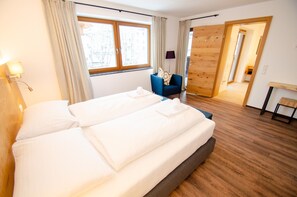 A hotel room with a large bed, a chair, a desk, and a wooden wardrobe.