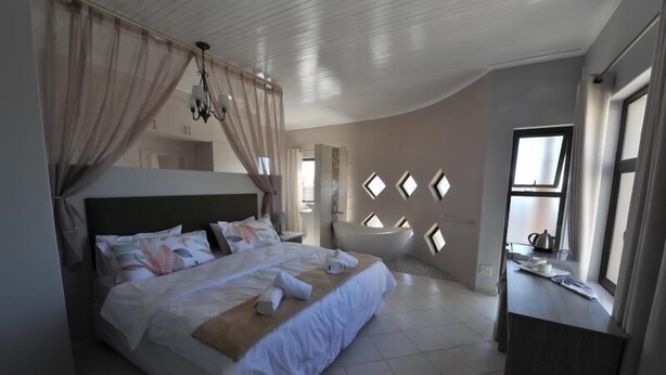 A bedroom with a large bed, a nightstand, a window with curtains, and a wall with geometric patterns. - Blue Lily Langstrand Self Catering (Walvis Bay)