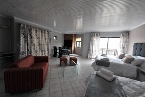 Une chambre d’h ôtel moderne comprenant un canapé, un lit, une table à manger avec des chaises et un balcon avec des rideaux.