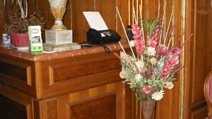 A wooden reception desk with a lamp, a telephone, a small potted plant, and a floral arrangement. - Hotel Il Fondaccio (Lizzano in Belvedere)