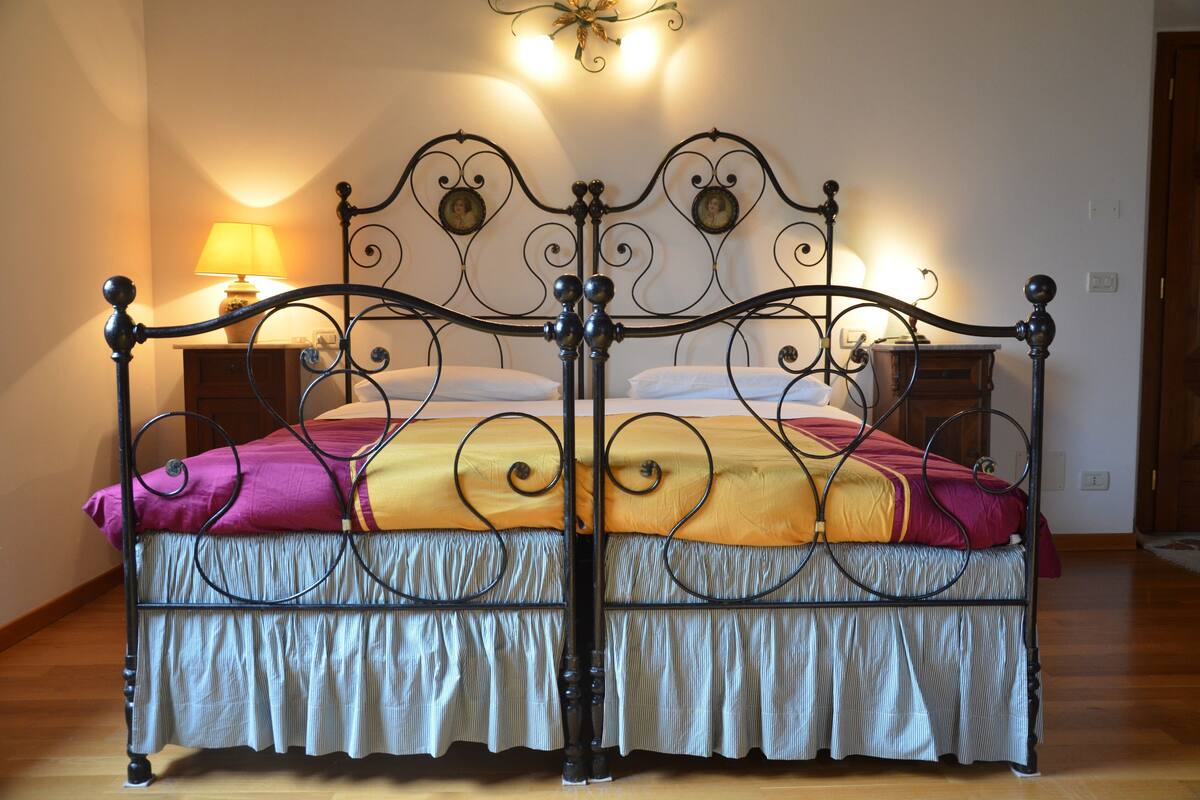 Una cama con dosel y dosel decorativo, una mesita de noche con lámpara y suelo de madera.