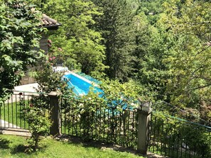 A swimming pool surrounded by a lush garden with a stone wall and metal fence. - Hotel Il Fondaccio (Lizzano in Belvedere)