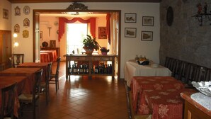 A dining area with multiple tables and chairs, a central table with a plant, and a view into another room. - Hotel Il Fondaccio (Lizzano in Belvedere)