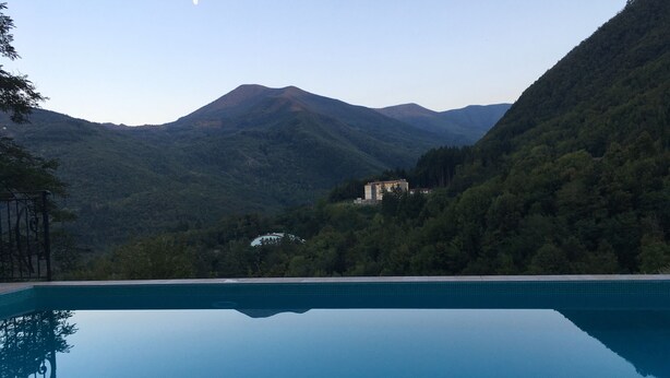 A clear blue swimming pool with a mountain backdrop and a building nestled among the trees. - Hotel Il Fondaccio (Lizzano in Belvedere)