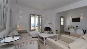 Una sala moderna con un sofá, una mesa de centro y una chimenea. Hay un comedor con una mesa y sillas. La habitación tiene ventanas amplias y vistas al exterior.