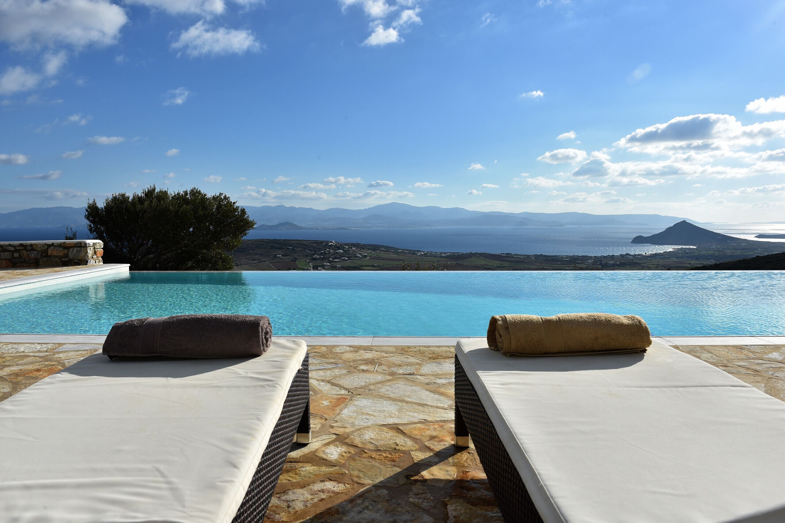 A poolside area with two lounge chairs and a stone-tiled floor.