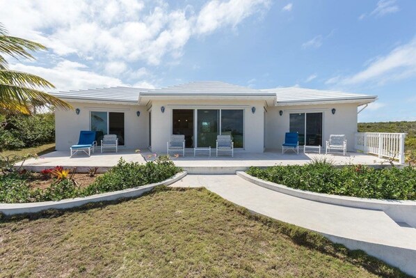 A modern two-story house with a covered patio, large sliding glass doors, and a well-maintained garden. - OceanWaves, A Vacation to Remember!A 1minute walk to private gazebo and beach. (Governor's Harbour)