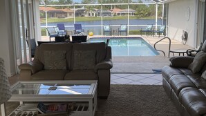 A covered patio area with a pool, seating, and a view of a residential area.