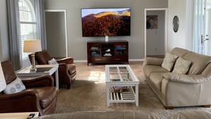 A living room with a large flat-screen TV, leather sofas, a coffee table, and a bookshelf.