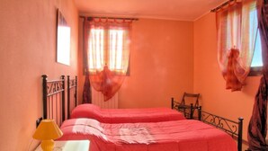A bedroom with two beds, a nightstand with a lamp, and a window with curtains. - Spring Apartment (Agriturismo Il Melograno) (Venezia)