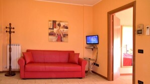 A room with a red sofa, a painting on the wall, a television, and a radiator. - Spring Apartment (Agriturismo Il Melograno) (Venezia)