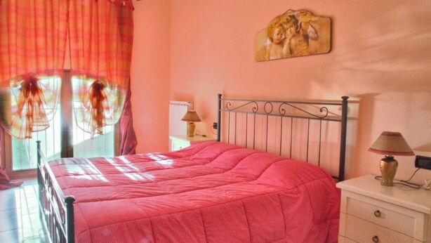 A bedroom with a bed, a nightstand, a lamp, a painting on the wall, and a window with curtains. - Spring Apartment (Agriturismo Il Melograno) (Venezia)