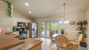 A modern kitchen with a central island, a dining area with wicker chairs, and a view of a pool through glass doors. - deal for remote working/studying and native plants/wildlife watching (Cape Coral)