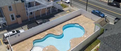 A swimming pool with a wavy design, surrounded by a concrete deck and a white fence.