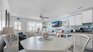 Een eetgedeelte met een witte tafel en stoelen, een plafondventilator en uitzicht op buiten.