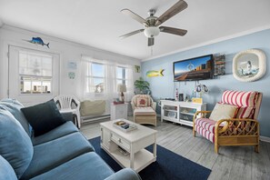 Ein Wohnzimmer mit einer Couch, Sesseln, einem Couchtisch, einem Fernseher und einem Deckenventilator.
