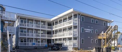 A multi-story hotel with a balcony on the second floor, a parking lot in front, and construction materials nearby.