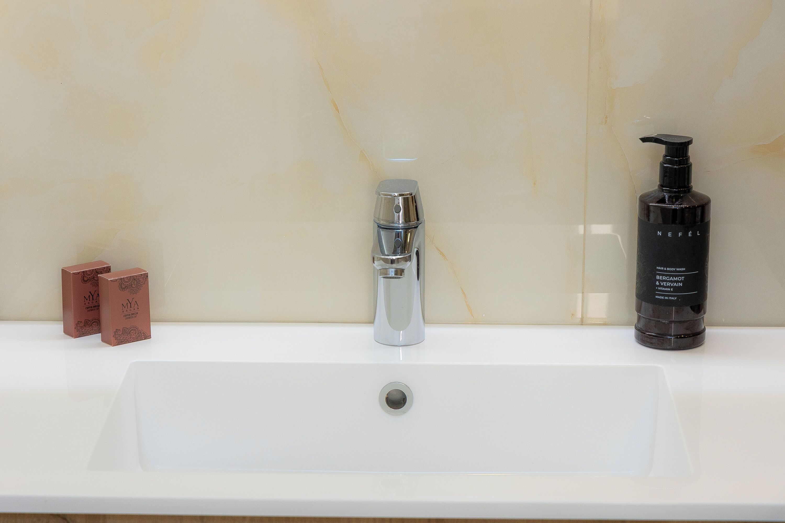 A bathroom sink with a modern faucet, a bottle of Neffel skincare product, and two small boxes.