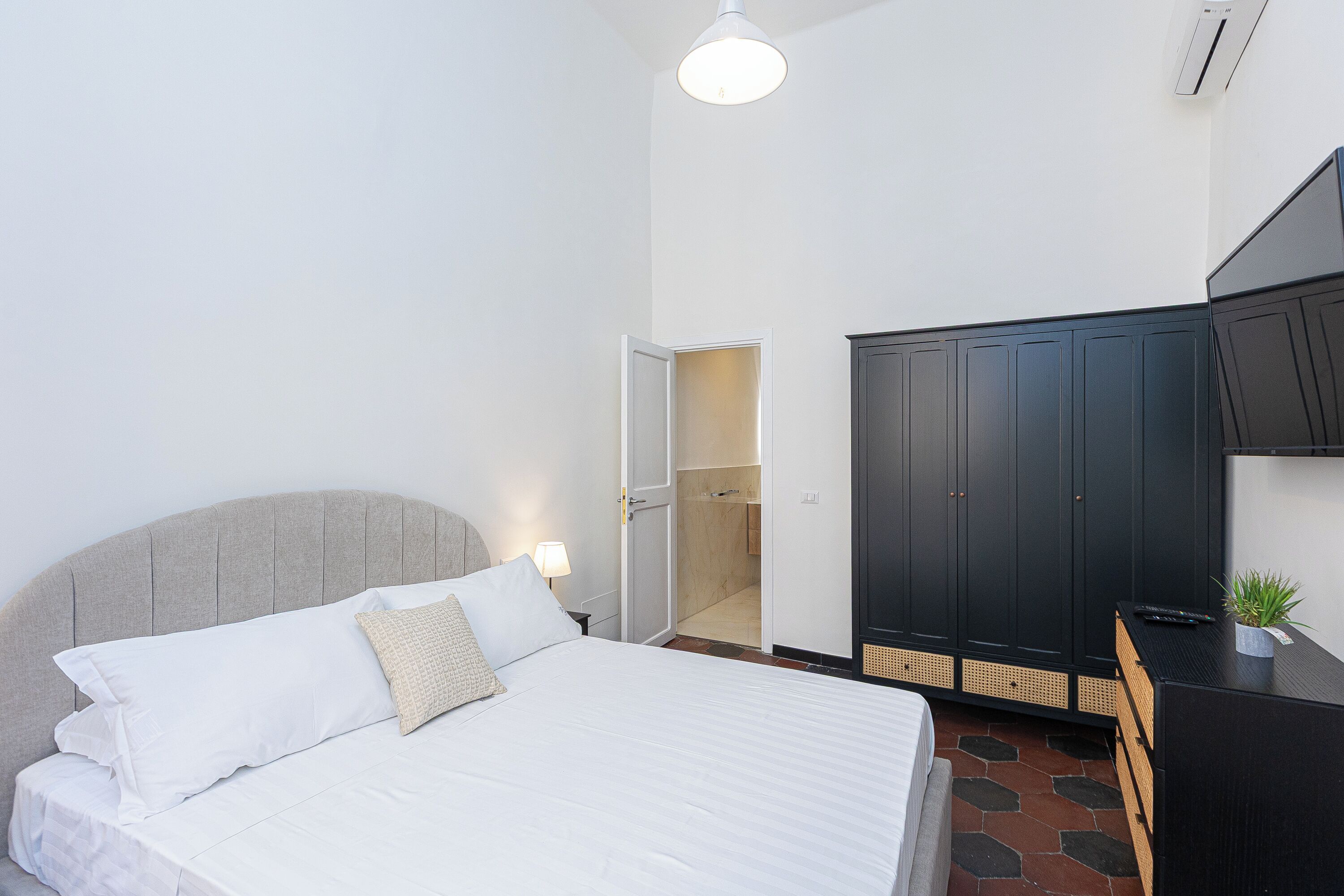 A bedroom with a bed, bedside table, lamp, wardrobe, and a small plant.
