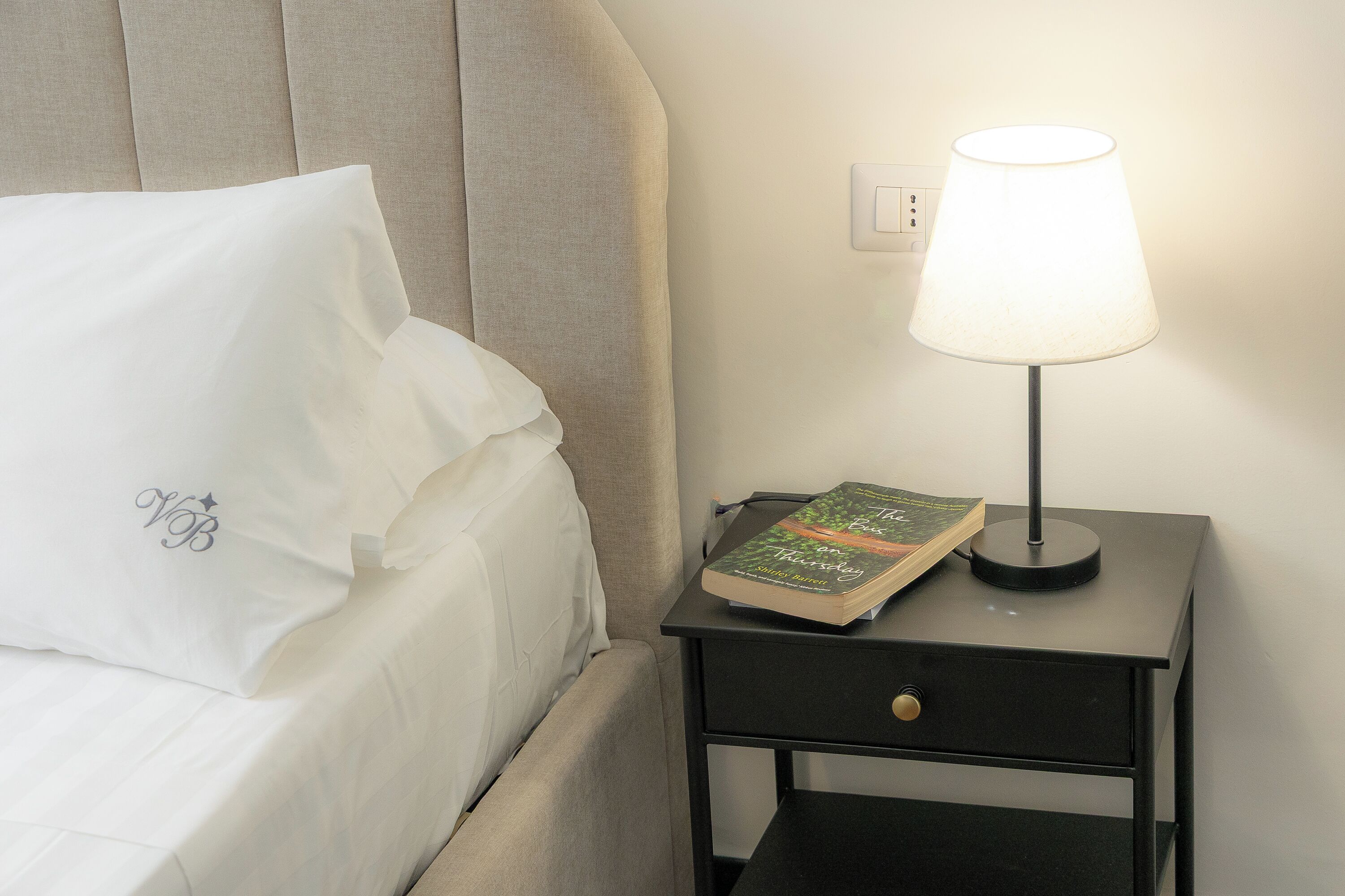 A neatly made bed with a white pillow and a book on a bedside table.