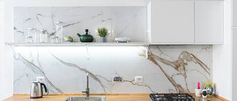 A modern kitchen with a marble backsplash, stainless steel appliances, and a wooden countertop.