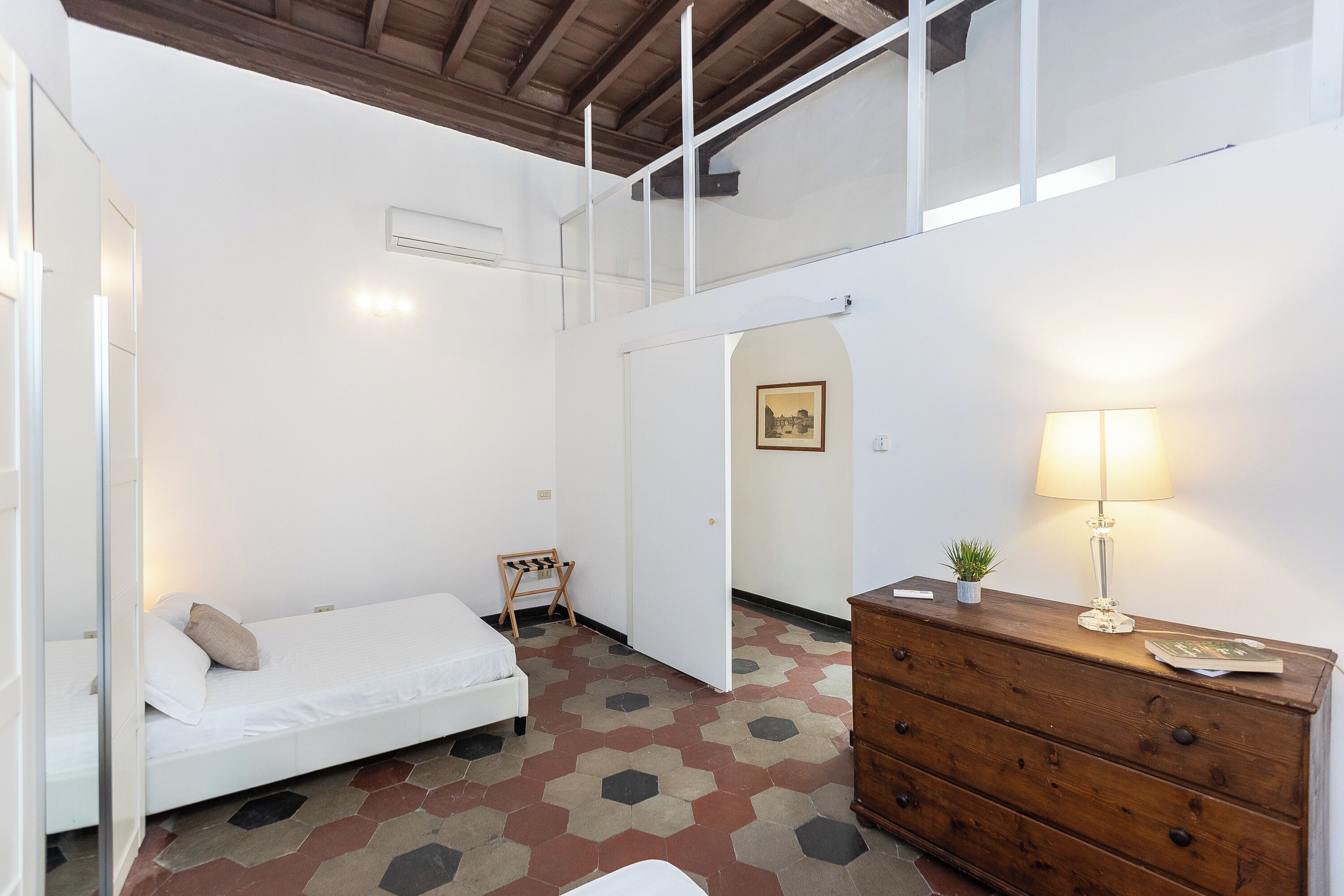A room with a bed, a dresser, a lamp, and a small table with a plant.